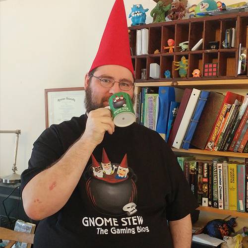 A man with a red gnome hat, a green Gnome Stew Mug raised to his lips, and wearing a black Gnome Stew t-shirt.