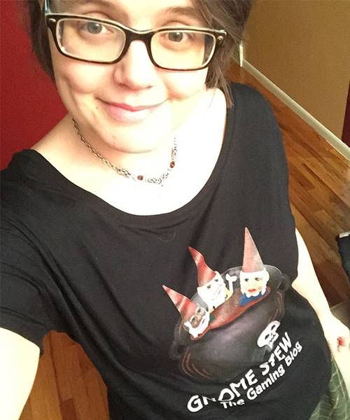 A woman being photographed from a high angle, showing from her eyes to her waist. She is wearing a black Gnome Stew t-shirt.